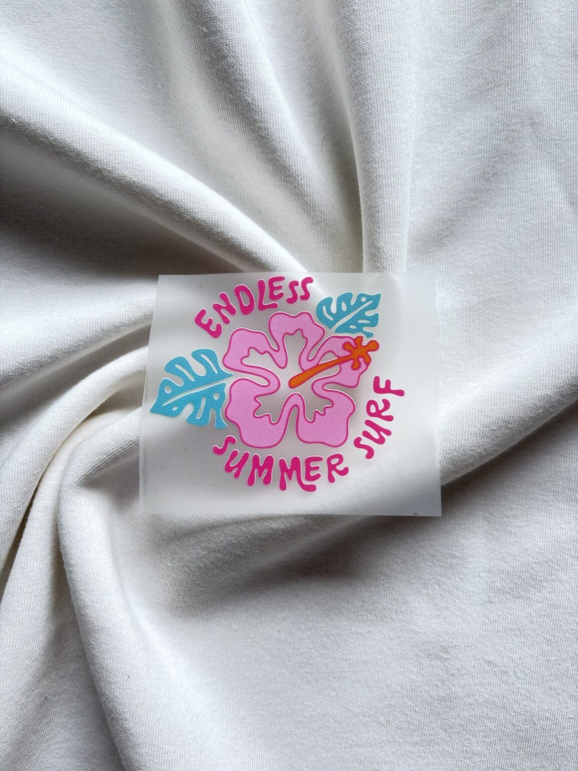Kleurrijke sticker met roze hibiscusbloem en tekst Endless Summer Surf op witte stoffen ondergrond