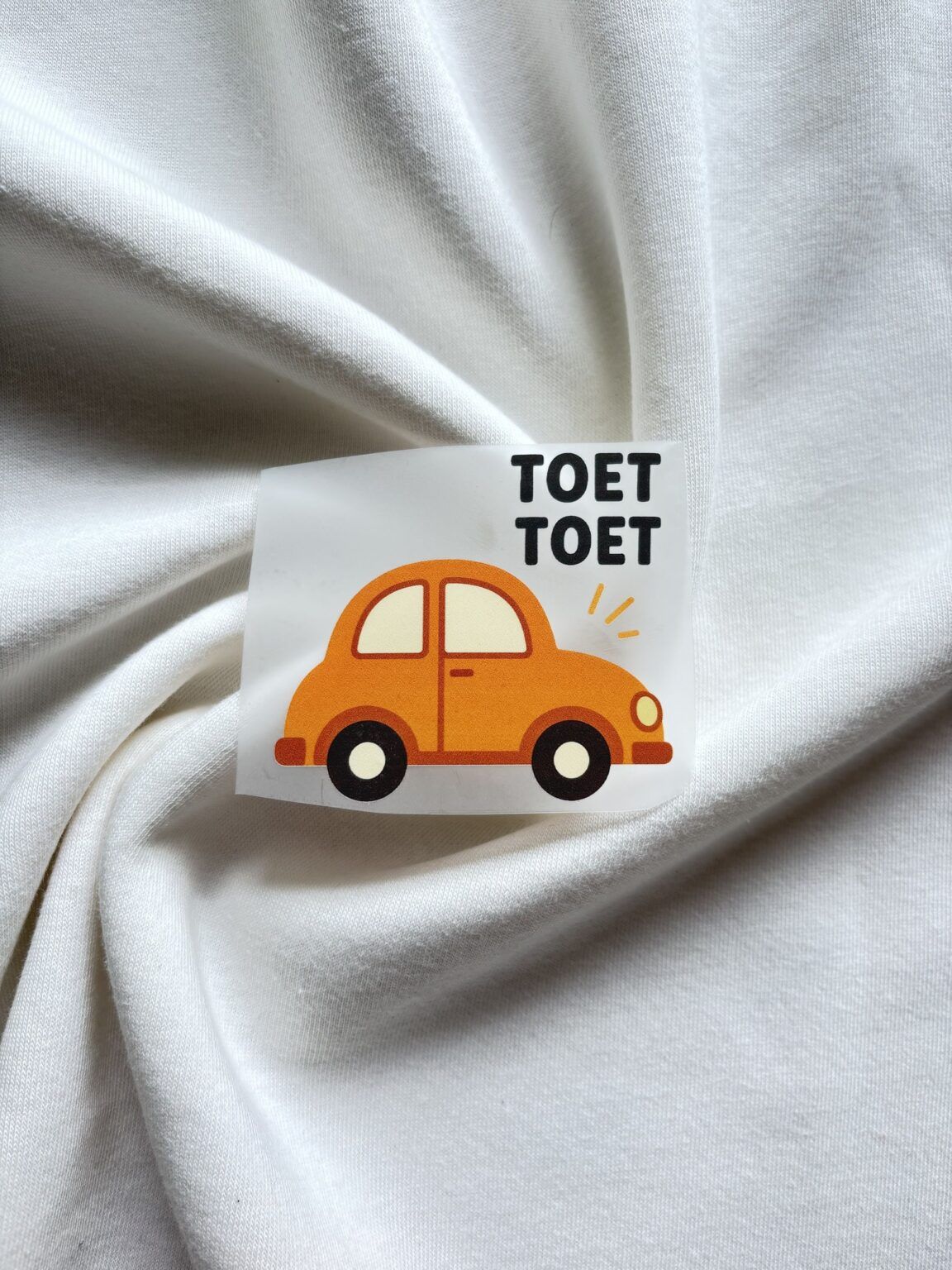 Kinderkaart met oranje auto en tekst 'TOET TOET' op witte stof achtergrond