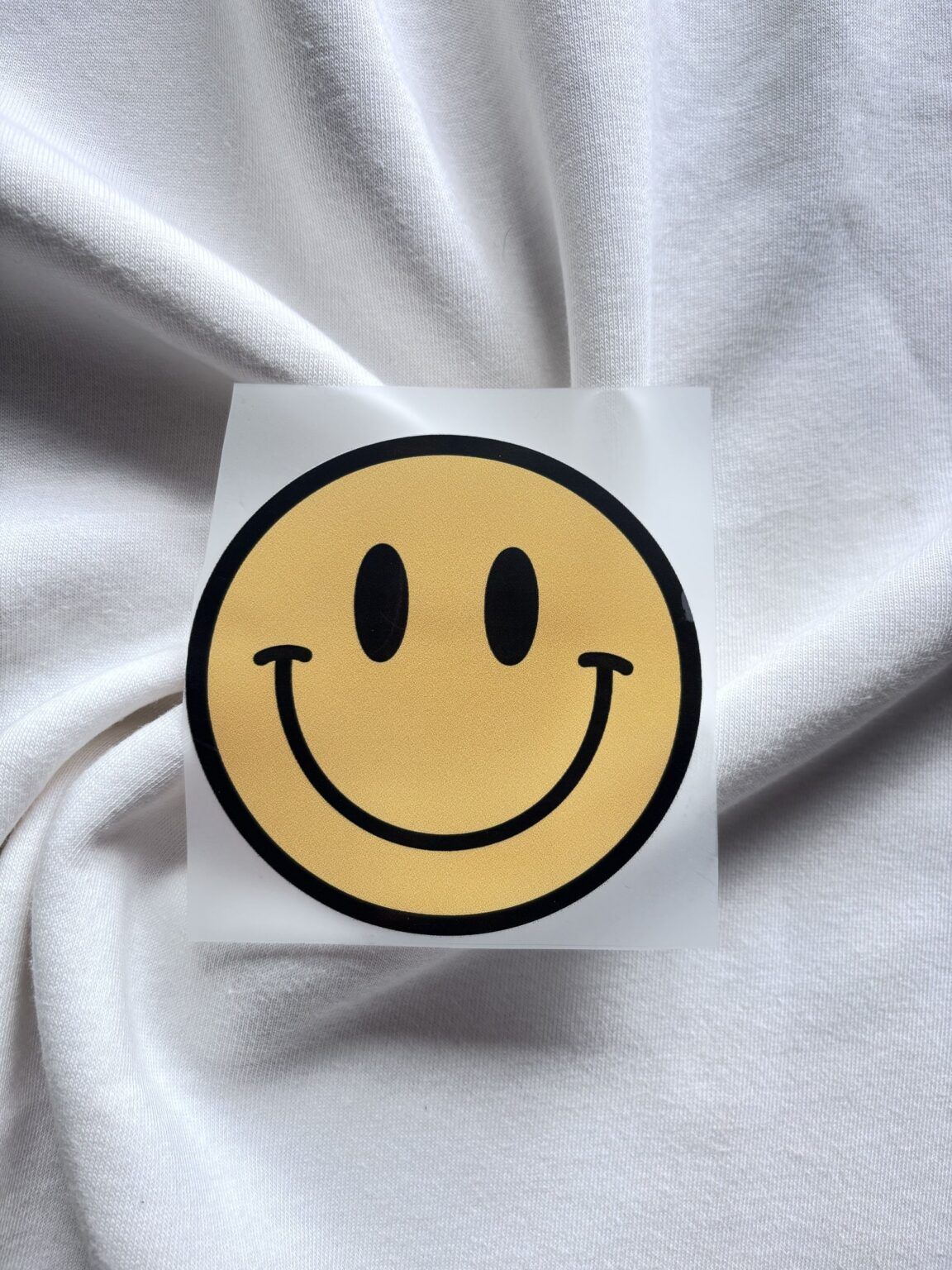 Gele smiley sticker op wit katoenen T-shirt met geplooide stof