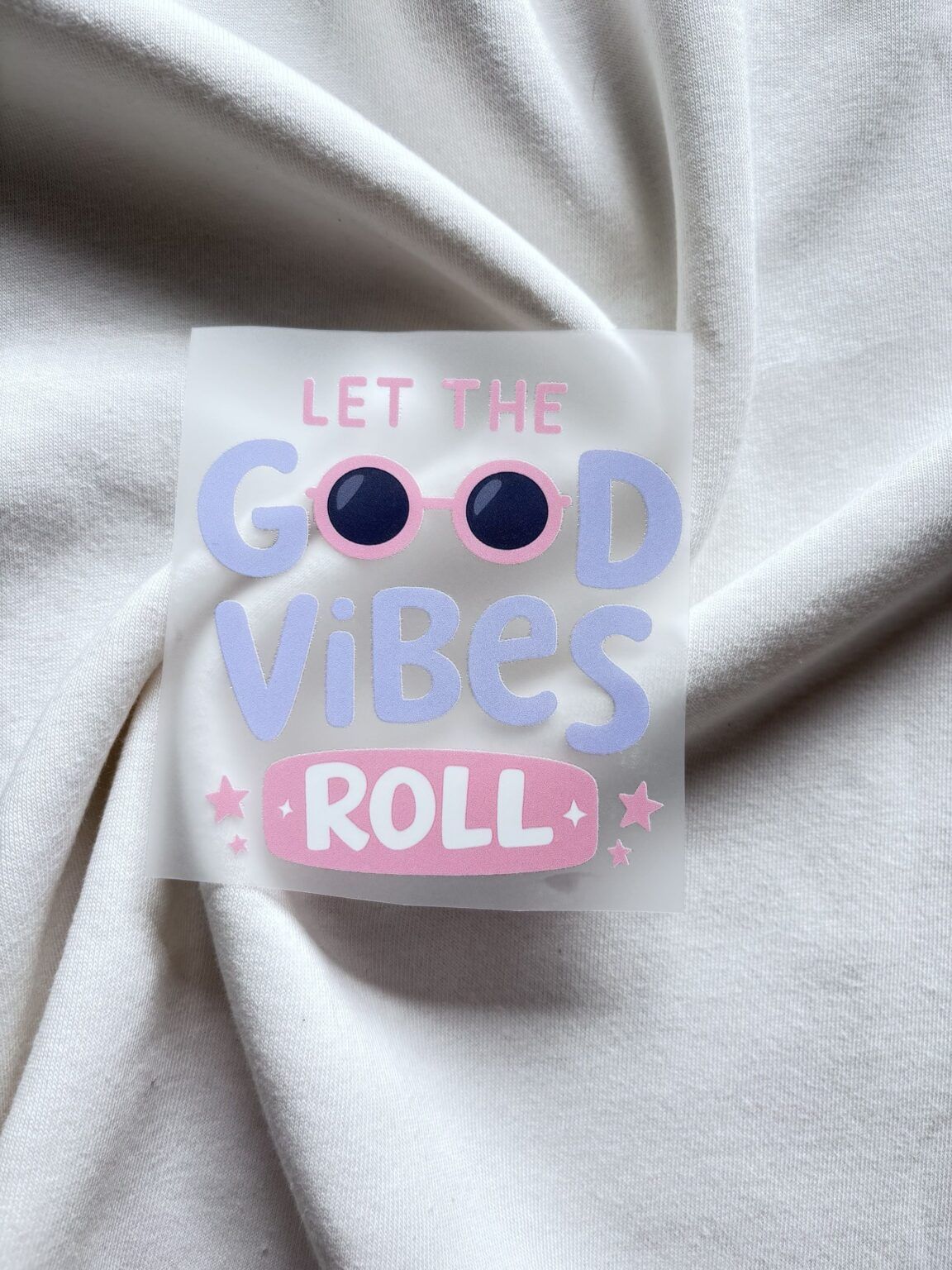 Sticker met roze zonnebril en tekst Let The Good Vibes Roll op beige gebreide stof achtergrond